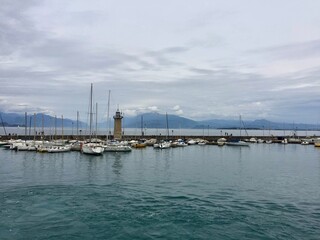 Cloudy weather on Garda lake, Italy. Picturesque spot in Desenzano del Garda. Yacht, lighthouse, pier, mountains on a background 