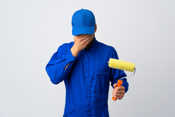 Painter man holding a paint roller isolated on white background with tired and sick expression