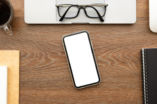 Smartphone with blank mockup screen is on top of wood office desk table with supplies. Top view with copy space, flat lay.