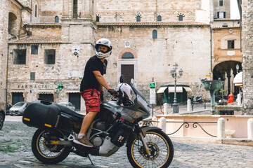 Fototapeta premium Handsome man in white helmet sitting on old adventure motorbike. Travel and vacation concept. Freedom. Narni, Italy