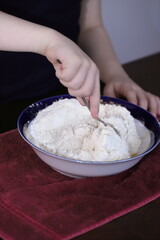 the child helps in the kitchen, the boy's hands knead dough in a bowl with a fork, we prepare delicious pastries