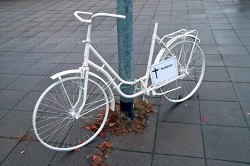 Fototapeta na wymiar ghost bike memorial with a cross sign for a killed cyclist at Frankfurt Main, Germany streets on a rainy Dreary Day. White ghost bicycle, memorial to a cyclist who died in traffic accident