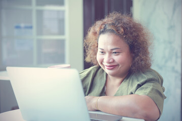 Asian Businesswomen adult sitting smiled happily have high self-confidence holding pink mug coffee looking at the laptop on a table at the house.