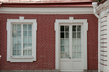 White framed windows and doors in the wall of the red brick house. Vintage glass windows of the old building. Classicism in architecture.