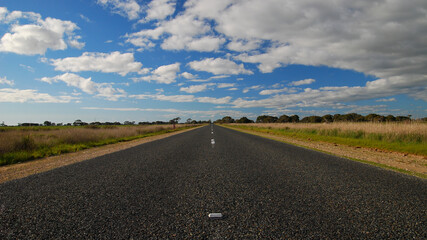 Long straight outback road with blue sky and some clouds