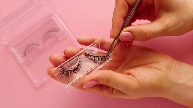 woman hand takes false eyelashes  using tweezers fashion and makeup on pink background