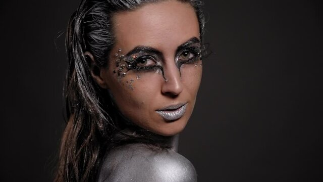 Portrait of a female model with silver skin and makeup on a black background.