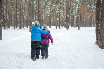 Fototapeta na wymiar In winter, brother and sister walk through the snowy forest.