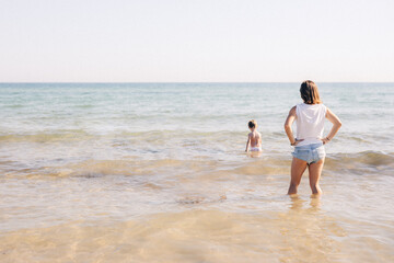 Fototapeta na wymiar Maman surveille son fils qui se baigne dans la mer en vacances sur la plage en été.