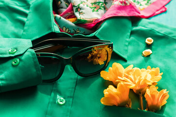 Background with fashionable clothes. Green trendy shirt and glasses with a bouquet of flowers. Beauty and style blog concept.