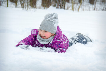 In winter, on a bright sunny day, a happy girl lies in the snow.