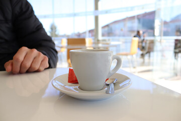 A cup of coffee on a table in a cafe against the background of a male hand and a silhouette of a guest.