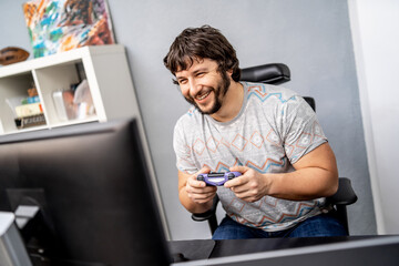 Cheerful man playing video or computer games in front of monitor in light wide room.