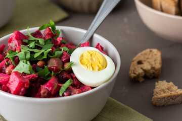 Russian salad vinaigrette in plates with boiled egg and black bread, salad of boiled and pickled vegetables and canned green peas