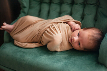 Newborn baby lying in the green sofa under the blanket