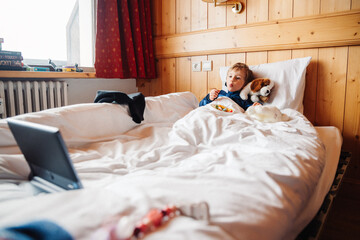 petit garçon regarde dessin animé sur sa tablette en mangeant des bonbons dans son lit en...