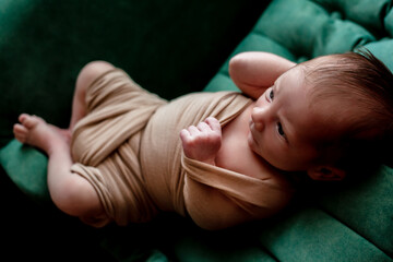 Newborn baby lying in the green sofa under the blanket