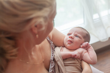 Young mother holding on hands  newborn two weeks baby at home in the room. Home portrait of  happy fаmily