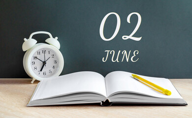 june 02. 02-th day of the month, calendar date.A white alarm clock, an open notebook with blank...