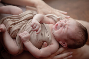 Young mother holding on hands  newborn two weeks baby at home in the room. Home portrait of  happy fаmily against the window