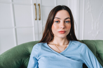 Portrait of attractive pretty young woman in casual clothing sitting on a sofa and looking on...