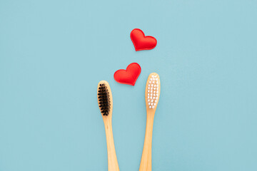 Two bamboo toothbrushes with a red heart on a blue background with copy space. Valentine's Day. Biodegradable bamboo, eco-friendly, waste-free and plastic-free toothbrushes. Top view, flat lay