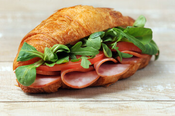Croissant sandwich with ham, tomato slices and arugula leaves and corn salad.  Wooden table.  Close-up. Macro photography.