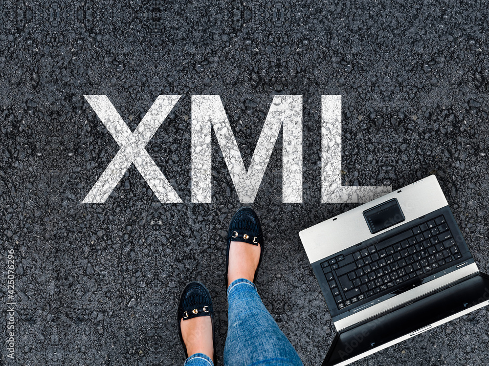 Aufkleber extensible markup language. man legs in shoes next to laptop and word xml on asphalt