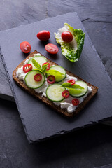 Fresh spring sandwich on a sliced gluten free sunflower bread. Red and green vegetables on black slate. Cucumber, chili and cottage cheese garnished with tomato and green leaves