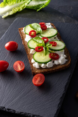 Fresh spring sandwich on a sliced gluten free sunflower bread. Red and green vegetables on black slate. Cucumber, chili and cottage cheese garnished with tomato and green leaves