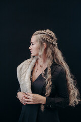 A beautiful girl of blonde nordic appearance with long hair in a black dress with fur.