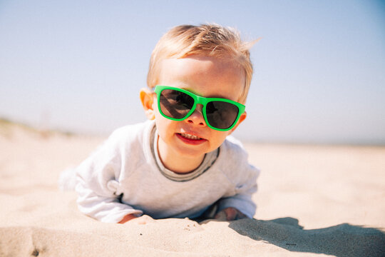 Gros plan d'un enfant couché à plat ventre dans le sable avec des lunettes de soleil