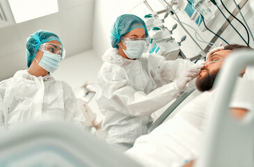 Doctors in protective suits, goggles and masks are monitoring the condition of a patient with...