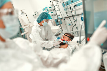 Doctors in protective suits put on a ventilation mask on a sick man with coronavirus disease...