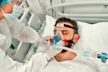 Doctors in protective suits put on a ventilation mask on a sick man with coronavirus disease...