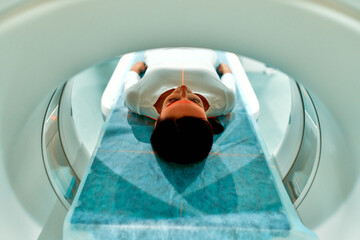Portrait of a patient lying on CT or MRI, the bed moves inside the machine, scanning her body and...