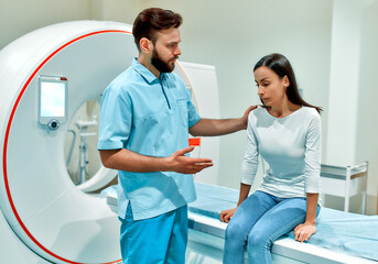 A caring radiologist consoles an agitated patient while sitting on a CT or MRI machine. In a medical laboratory with high-tech equipment.