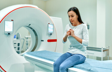 An agitated, sad and frightened patient sits on the bed of a CT or MRI machine. In a medical...