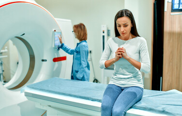 An agitated, sad and frightened patient sits on the bed of a CT or MRI machine. In a medical...