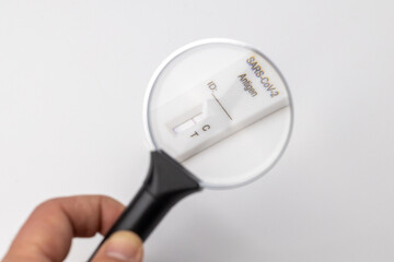 Close-up of a negative Covid-19 antigen test. a hand holds a magnifying glass over a negative...