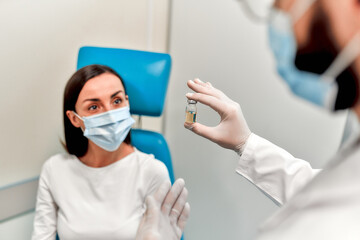 Vaccination, immunization campaign, disease prevention concept. A woman wearing a medical mask receives the Covid-19 vaccine in a doctor's office. The nurse talks about the vaccine to the patient.