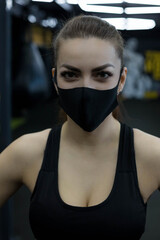 Female athlete in black face mask have break between exercises in gym