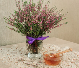 A bouquet of lilac heather in a vase and a bowl of honey