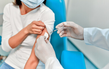 Vaccination, immunization campaign, disease prevention concept. Young woman in medical face mask getting Covid-19 vaccine at doctor's office. Professional nurse giving flu injection to patient