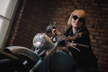 Fototapeta na wymiar Happy woman motorbiker in a sunglasses is sitting on the old motorcycle.