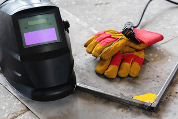 Welding helmet, gloves and metal frame on the floor background.