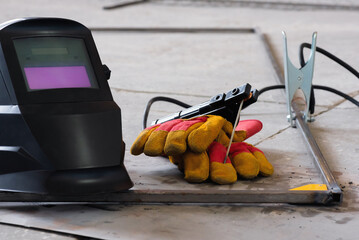 Welding helmet, gloves and metal frame on the floor background.