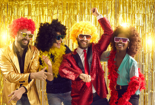 Happy people dancing gangnam style on stage with shiny golden background. Group of friends disguised in boas, glasses, sequin jackets and funny silly curly wigs having fun at night club disco party