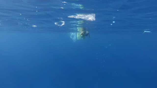 Woman collects plastic garbage underwater clean up of a dirty discarded plastic bags, bottles, cups and other plastics waste floating in the sea. Snorkeler catches plastic trash from the water