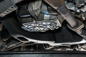 Oil drains from from beneath vehicle during a routine maintenance fluid change at mechanic garage.